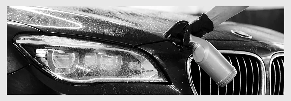 Hand applying polish from a bottle onto the bonnet of a dark car near the headlight.